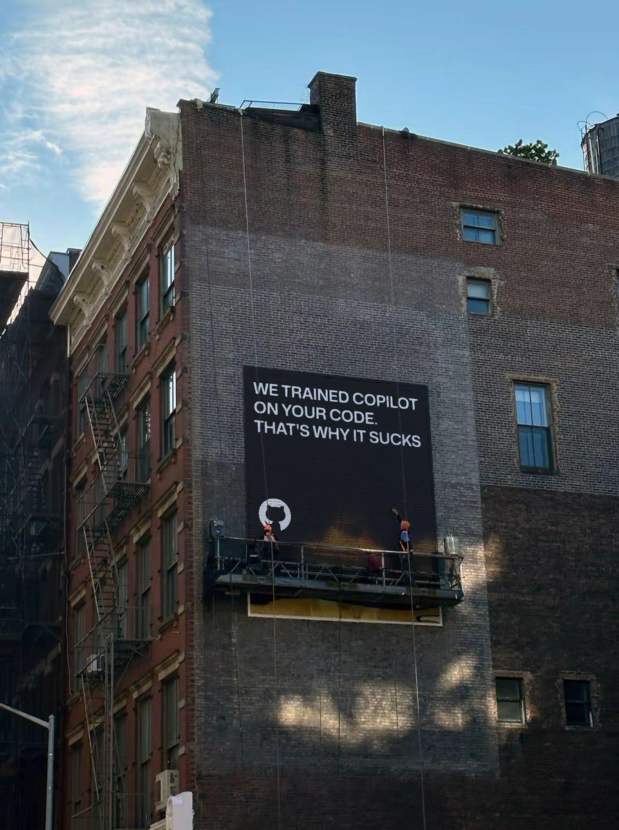 Billboard on a house joking about Github copilot code generation quality. Words on a billboard: "We trained copilot on your code. That's why it sucks"